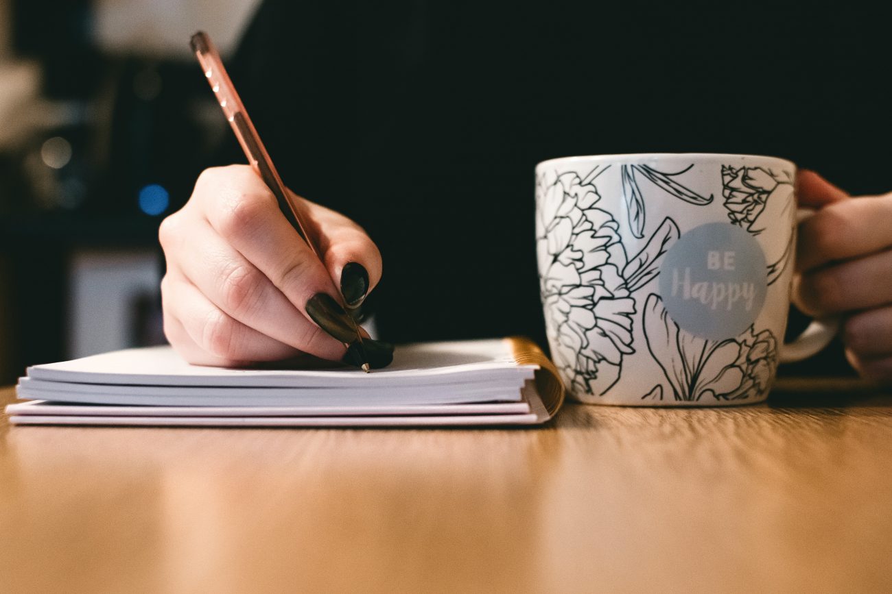 person writing next to coffee cup